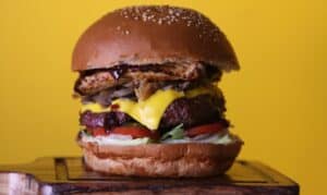 Hamburger artigianale con carne, formaggio fuso, insalata e pane ai semi su sfondo giallo